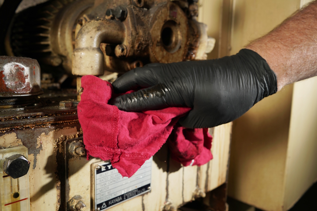 gloved hand with a rag wiping down machinery